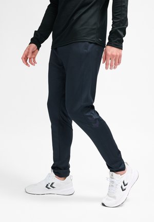 Marineblauwe sportbroeken met een gestructureerde afwerking, slim fit, met een logo-accent. Gepaard met witte hardloopschoenen met zwarte details.