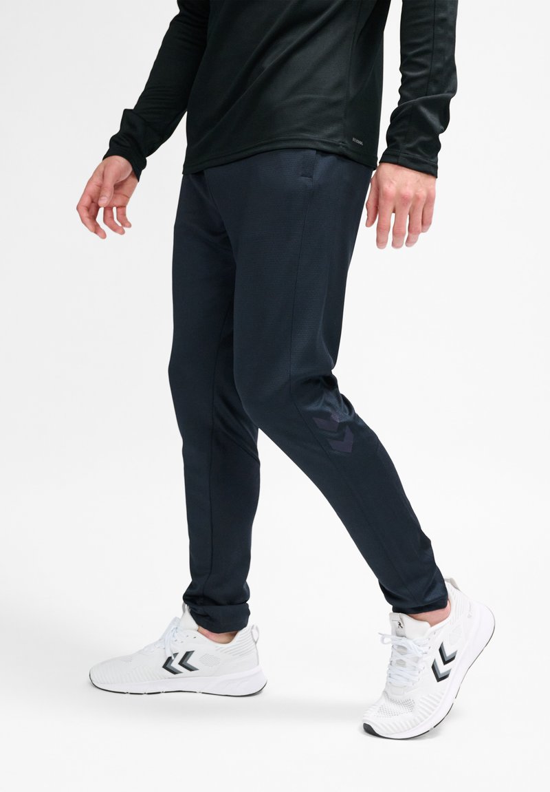 Marineblauwe sportbroeken met een gestructureerde afwerking, slim fit, met een logo-accent. Gepaard met witte hardloopschoenen met zwarte details.