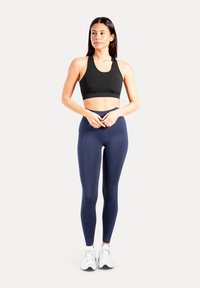 Zwarte sportbh en marineblauwe leggings gemaakt van rekbare stof. De leggings hebben een zijzak; beide items zijn ontworpen voor sportief gebruik.