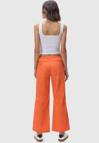 Orange wide-leg pants with an elastic waistband and back pockets, paired with a white tank top. Footwear features a contrasting black and white design.