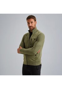 Olivno zelena zip-up jopica z teksturiranimi rokavi iz pletenice, sprednji žep z zadrgo in rebrastim ovratnikom. Ima prilegajočo se zasnovo in mehak material.