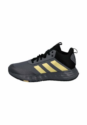 Zapatilla deportiva en negro y gris con tres rayas amarillas, parte superior de malla y suela de goma texturizada. Incorpora cordones y una pestaña trasera.