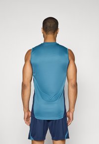 Haut de sport sans manches en bleu avec une texture lisse, associé à un short bleu foncé. Le design présente des accents latéraux contrastés.