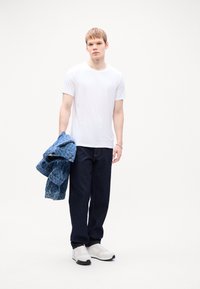 Hvit t-skjorte, mørkeblå jeans og hvite joggesko. En blå denimjakke holdes over den ene armen. Enkel, uformell design med minimale detaljer.