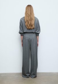 Szary zestaw odzieży domowej składający się z luźnej bluzy z paskowanymi ściągaczami oraz spodni o szerokich nogawkach. Miękki materiał o gładkiej teksturze.