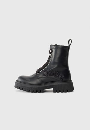 Botte de combat en cuir noir avec semelle épaisse, lacets noirs, tirette à l'arrière et "DSQ2" brodé sur le côté.