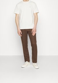 Krémové bavlněné tričko s krátkým rukávem, doplněné o hnědé texturované kalhoty a bílé tenisky s barevnými oky.