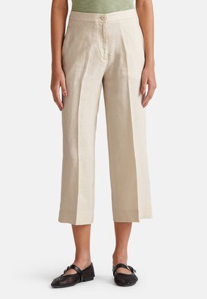 Pantalons larges en lin beige avec fermeture à bouton devant et plis, présentant une longueur raccourcie et des ourlets roulés. Assortis avec des chaussures tissées noires.