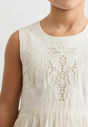 Krēmkrāsas kleita ar smalku baltu izšuvumu ziedu motīviem uz krūškurvja un savākta tilla svārku malā.