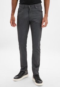 Szare dopasowane spodnie o fakturowanym wykończeniu, z zapięciem na guzik i zamek błyskawiczny, w wąskim kroju. Noszone z czarnymi trampkami.