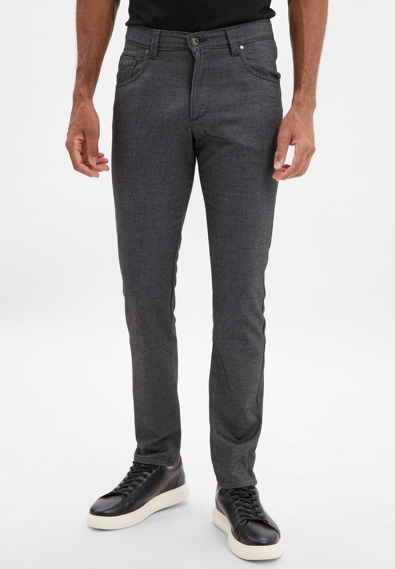 Szare dopasowane spodnie o fakturowanym wykończeniu, z zapięciem na guzik i zamek błyskawiczny, w wąskim kroju. Noszone z czarnymi trampkami.