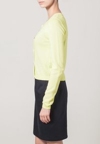 Helle gelbe Strickjacke aus weichem Material, mit langen Ärmeln, einem gerippten Saum und Knopfverschluss, kombiniert mit einem dunklen Rock.