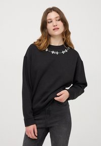 Czarna bluza z długimi rękawami, z dekoracyjnym haftem kwiatowym wzdłuż dekoltu. Wykonana z miękkiego materiału, o luźnym kroju.