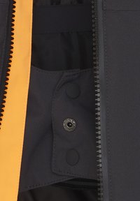 Svart zip-jacka med insidan i ljus orange som har svarta tryckknappar och en slät textur. Dragkedjebandet är synligt längs kanten.