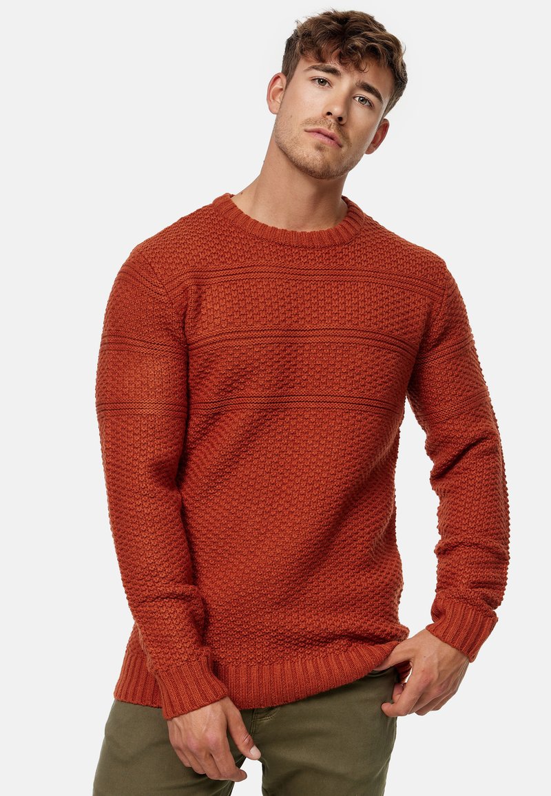 Jersey de color óxido tricotado con patrones texturizados, puños y dobladillo de canalé. Presenta un diseño clásico de cuello redondo y un ajuste relajado.