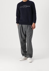 Sweatshirt bleu marine avec logo blanc, pantalon plissé gris et baskets blanches. Design décontracté avec col rond et manches longues.