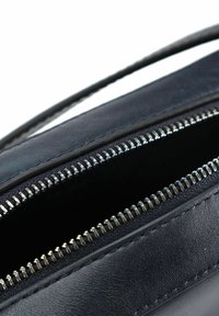 Borsa in pelle nera con apertura zip con denti di metallo. Texture liscia, forma sottile e design minimalista. Nessun marchio visibile.