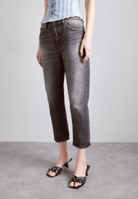 Jeans cropped in denim grigio con un leggero sbiadimento e orlo sfrangiato. Abbinati a sandali neri con dettagli metallici.
