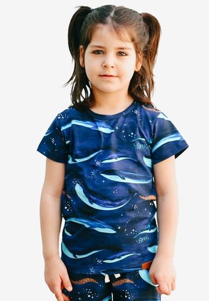 Young girl with brown hair in pigtails wearing a navy blue shirt and pants with a dolphin and starry ocean pattern.