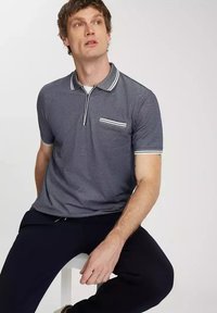 Szary polo z wąskim kołnierzykiem w białe paski, krótkim rękawem i kieszenią na piersi z poziomym detalem w białe paski.