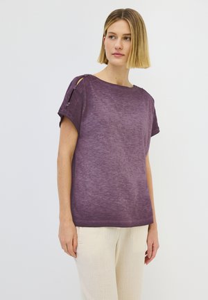 Haut violet à manches courtes avec une coupe décontractée, orné de boutons sur les épaules et en tissu doux et texturé. Assorti à un pantalon clair.