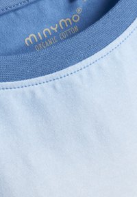 Lichtblauw organisch katoenen shirt met een ronde hals en contrasterende blauwe ribbels; heeft een zachte textuur en zichtbare stiksels.