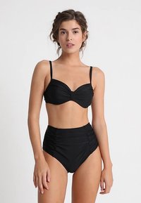 Musta biksupuku, jossa on ryppyperäinen korkeavyötäröinen alaosa ja toppi, jossa on pehmustettu ja kiertoreunainen etuosa. Säädettävät olkaimet. Sileä, joustava kangas.