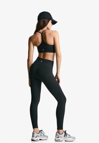 Crni sportski top s dizajnom racerback, uparen s crnim tajicama visokog struka. Srebrne tenisice upotpunjuju odjevnu kombinaciju.