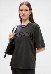 Σκούρο γκρι κοντομάνικο μπλουζάκι με τη λέξη "ΕΛΕΥΘΕΡΙΑ" σε έντονη μαύρη γραμματοσειρά, με άνετη εφαρμογή και στρογγυλή λαιμόκοψη.