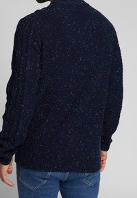 Granatowy sweter z dzianiny z kolorowymi plamkami, z teksturowanym splotem na rękawach, ściągaczem przy kołnierzu i u dołu, w luźnym kroju.