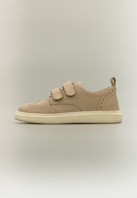 Μπεζ σουέντ αθλητικό παπούτσι με διπλές λουρίδες βέλκρο, διάτρητα διακοσμητικά μοτίβα και κρεμ λαστιχένια σόλα, εμφανίζεται από το πλάι σε ουδέτερο φόντο.