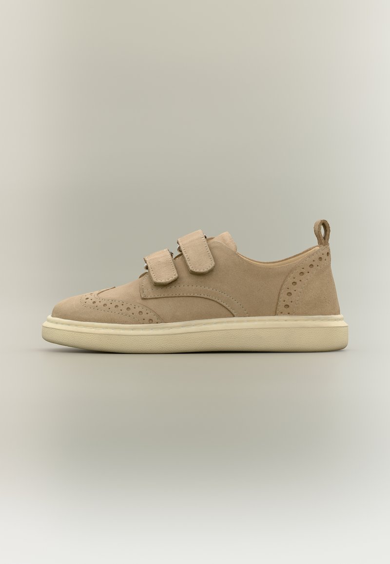 Μπεζ σουέντ αθλητικό παπούτσι με διπλές λουρίδες βέλκρο, διάτρητα διακοσμητικά μοτίβα και κρεμ λαστιχένια σόλα, εμφανίζεται από το πλάι σε ουδέτερο φόντο.