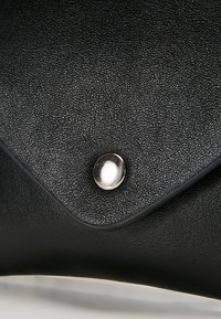 Borsa a mano in pelle nera con superficie strutturata, dotata di una chiusura a scatto lucida in argento su un pattina triangolare.