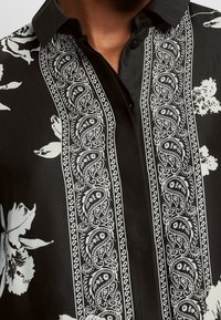 Zwarte shirt met witte bloem- en paisleypatronen, met een button-down kraag en een gestructureerde stof. Gedetailleerde stiksels aan de voorkant.
