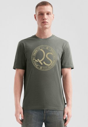 Olivegrünes T-Shirt mit kurzen Ärmeln aus Baumwolle, das ein großes ringförmiges gelbes grafisches Muster mit "RS" in der Mitte und strukturiertem Stoff zeigt.