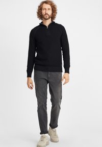 Maglione a collo zip di maglia nera, con tessuto testurizzato. Abbinato a pantaloni slim-fit grigi e sneakers beige chiaro.