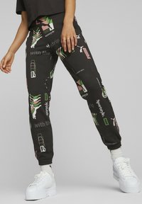 Svarta joggers med blandade grafiska tryck i rosa, grönt och vitt. Har elastisk midja, muddade anklar och en avslappnad passform.