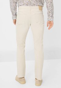 Beige gerade geschnittene Jeans aus Baumwolle mit Gesäßtaschen und einem Lederetikett am Bund, kombiniert mit beigen Schuhen.