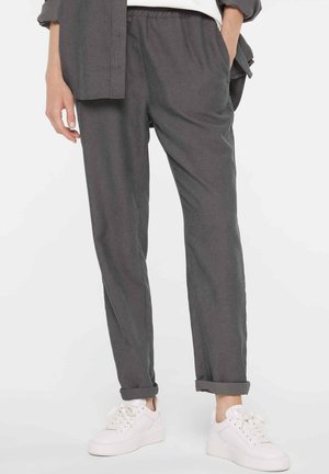 Lower body wearing dark gray corduroy pants with rolled cuffs, white sneakers, and a matching gray jacket with one hand in pocket.