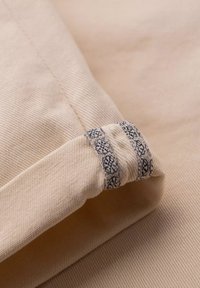 Tissu beige à texture côtelée, présentant un accent décoratif à motif bleu au niveau du poignet. Le tissu est lisse avec une finition douce.