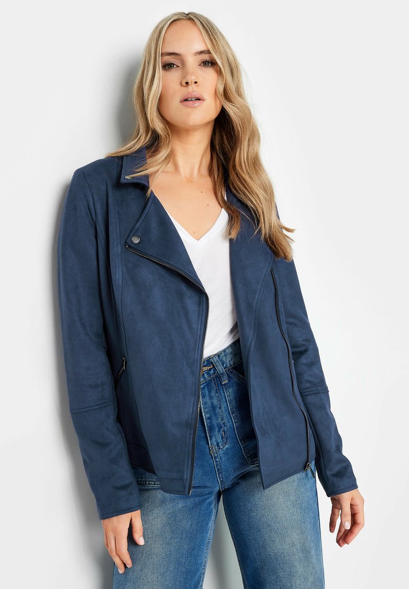Marinblå faux suede jacka med notchkrage, dragkedja och sidofickor, parat med en vit V-ringad topp och blå högmidjade jeans.