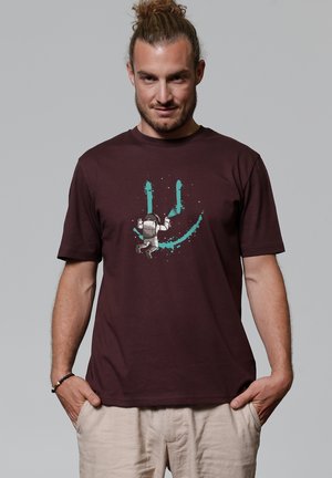 Maroon cotton t-shirt featuring a graphic of an astronaut and blue paint splashes, short sleeves, and a relaxed fit.