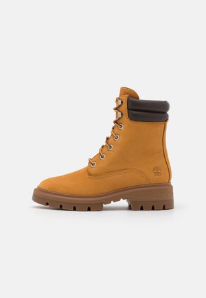 Brązowy i żółty zamszowy but z wyściełanym kołnierzem, metalowymi oczkami i masywną gumową podeszwą z głębokim bieżnikiem zapewniającym przyczepność.