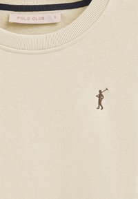 Sudadera de color crema con un cuello acanalado y una pequeña figura marrón bordada sosteniendo un objeto. La etiqueta dice "POLO CLUB", tamaño S.