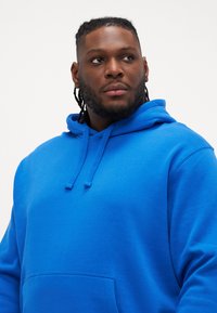 Sweatshirt azul com capuz feito de tecido macio, apresentando um bolso frontal, cordões e um corte descontraído.