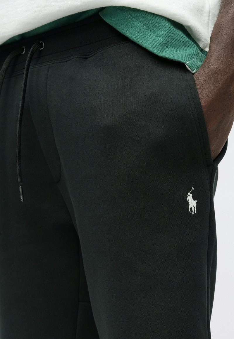 Pantaloni della tuta neri con vita elasticizzata e lacci, tasche laterali e un logo ricamato bianco di un giocatore di polo.