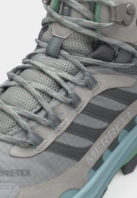 Εγγύς λήψη γκρι και ανοιχτού μπλε πεζοπορικού παπουτσιού Merrell με δίχτυ, κορδόνια με σχέδιο, επενδεδυμένη γλώσσα και ορατή υφή στη σόλα.