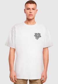 T-shirt en coton blanc à coupe décontractée, présentant un graphique en texte cursif noir "Baby Don't Cry" sur le côté gauche de la poitrine.