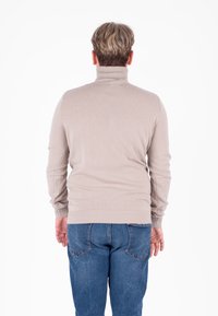 Maglione beige a collo alto con colletto e polsini a coste, vestibilità slim, indossato con jeans in denim blu, visto da dietro. Texture liscia.