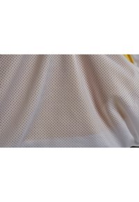 Mesh sportshirt met een witte stof met kleine hexagonale gaten, wat ademend vermogen biedt. Geribbelde oppervlak met gele accenten.